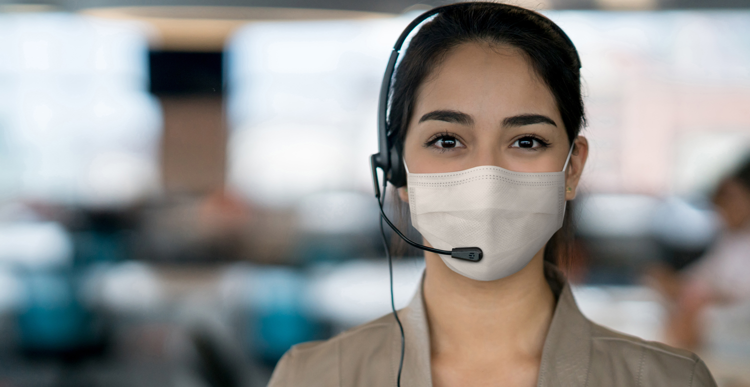 Woman wearing a facemask and a headset looking directly into the camera.