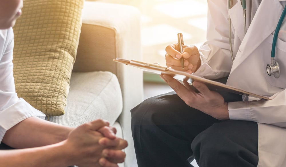 Doctor meeting with a patient while taking notes on a clipboard.